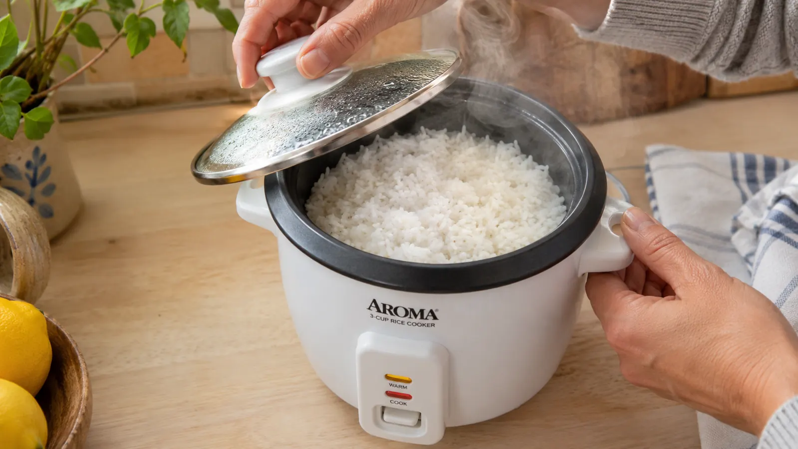 Hand lifting the lid of an Aroma rice cooker to reveal perfectly cooked rice steaming inside