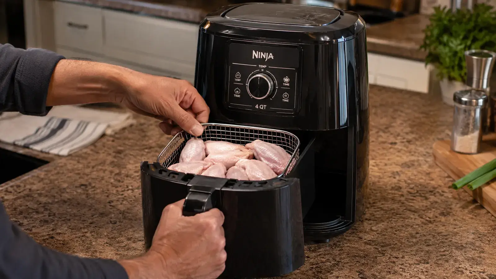 Hand placing frozen chicken wings into the Ninja air fryer basket